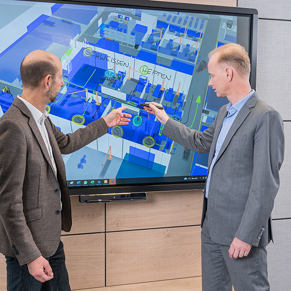 Andreas Knollmayr und Wolfgang Waldhäusl bearbeiten am Monitor das 3D-Modell einer Fabrik-Planung